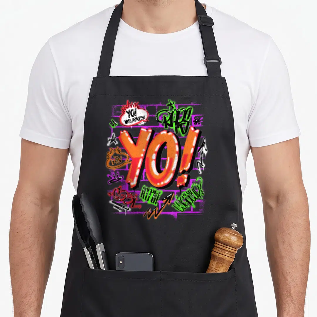 Rap hip hop apron - Graffiti text design with YO MTV RAPS and WASSUP in orange green red black — shown on a black cotton canvas apron against a white background