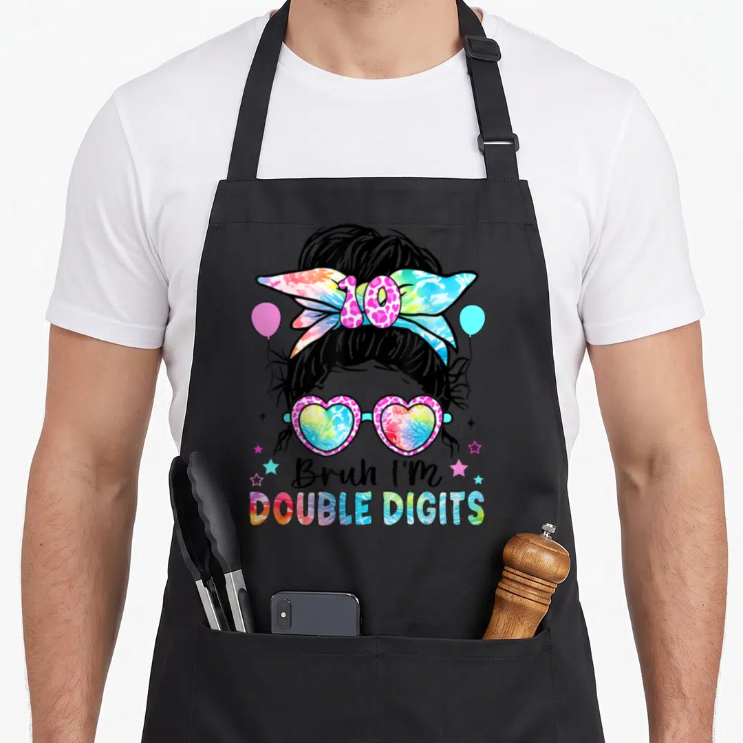 Bruh double digit 10th birthday apron - Cartoon messy bun girl with heart glasses, tie-dye bow, and stacked text — shown on a black cotton canvas apron against a white background