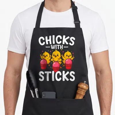 Fitness drum apron - Three yellow cartoon chicks playing red drums under CHICKS WITH STICKS text — shown on a black cotton canvas apron against a white background