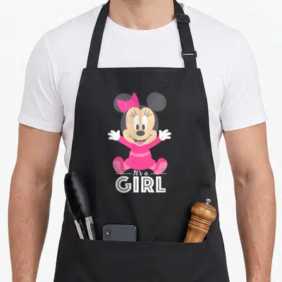 Baby tablet apron - Minnie Mouse in pink dress with It's a GIRL text on grey background — shown on a black cotton canvas apron against a white background