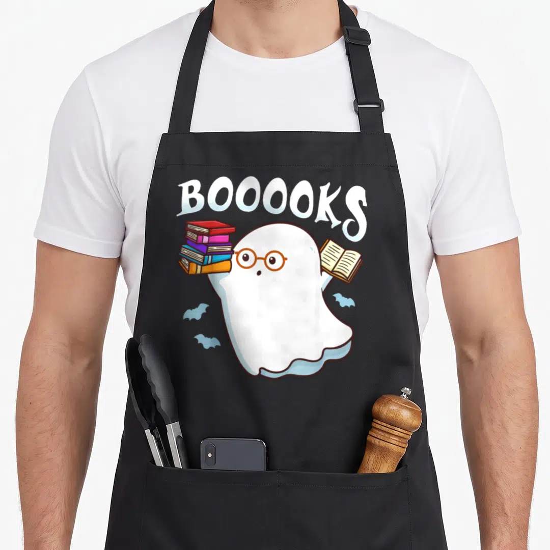 Book halloween apron - Ghost with brown glasses holding books under arched BOOOOKS text with two blue bats — shown on a black cotton canvas apron against a white background