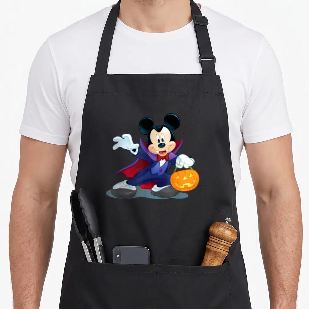 Vampire halloween apron - Mickey Mouse in purple vampire cape holding orange pumpkin bucket — shown on a black cotton canvas apron against a white background