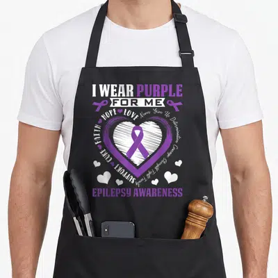 Month warrior epilepsy awareness apron - Purple heart with ribbon and white script text reading I wear purple for me — shown on a black cotton canvas apron against a white background