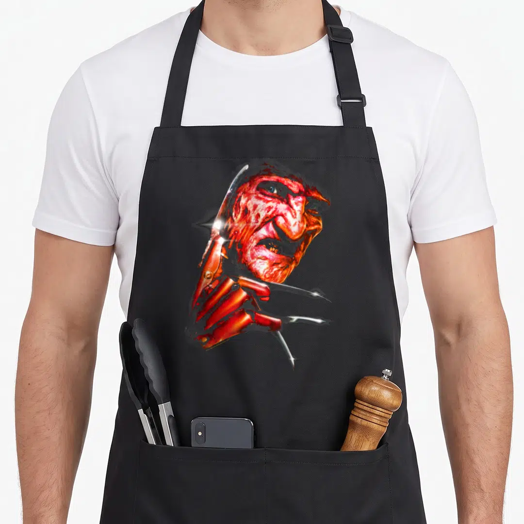 Nightmare face apron - Red monster head in profile with silver claw blades overlapping the left side — shown on a black cotton canvas apron against a white background
