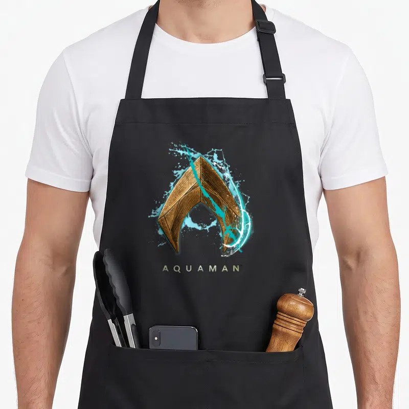 Movie worlds greatest apron - Gold Aquaman logo with blue and white water splashes and text below — shown on a black cotton canvas apron against a white background