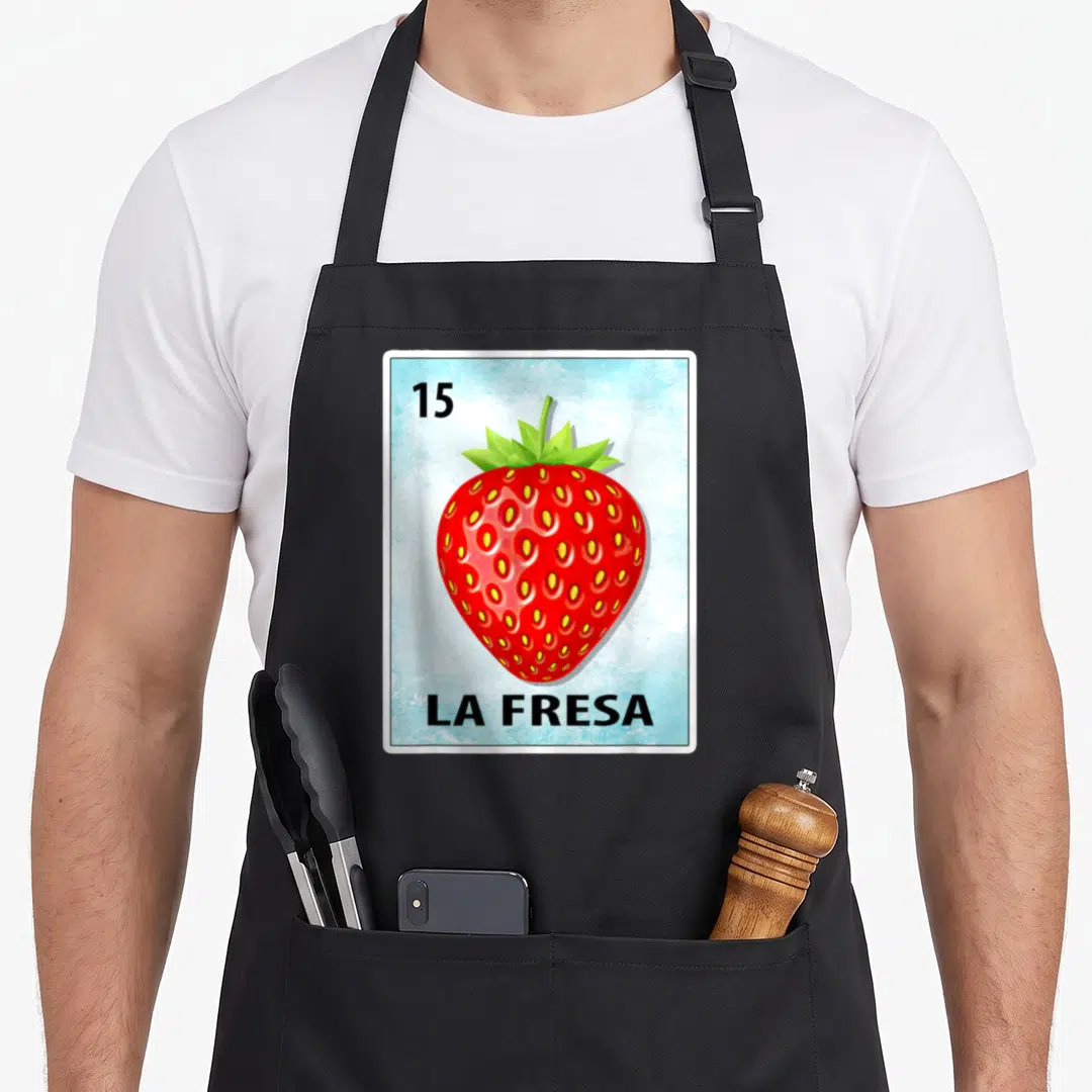 Fresa strawberry apron - Red strawberry on light blue card with 15 and LA FRESA text — shown on a black cotton canvas apron against a white background