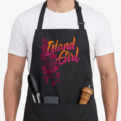 Flower guam aprons - Island Girl GUAM text over heart with palm tree, sailboat, and pink hibiscus flowers — shown on a black cotton canvas apron against a white background