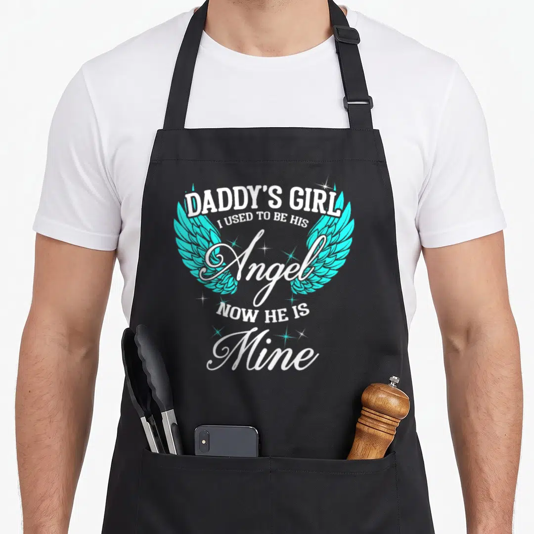 Guardian angels and aprons - Daddy's Girl text with turquoise wings and white stars surrounding the word Angel — shown on a black cotton canvas apron against a white background