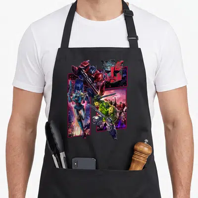 Cybertron transformer apron - Optimus Prime, Bumblebee, and Autobot logo in pink framed panels with red blue yellow — shown on a black cotton canvas apron against a white background