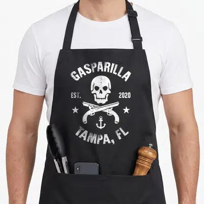 Gasparilla skull apron - White distressed skull crossed pistols anchor GASPARILLA 2020 TAMPA FL text — shown on a black cotton canvas apron against a white background