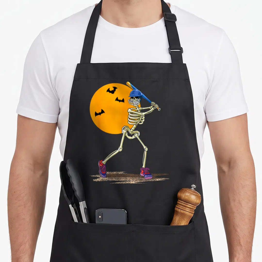 Baseball skeleton apron - Cartoon skeleton batter in blue helmet holding bat in front of orange moon with bats — shown on a black cotton canvas apron against a white background