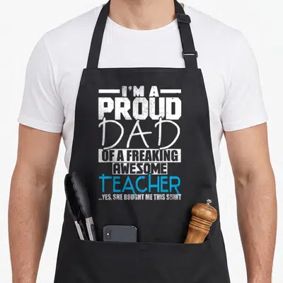 Proud personalized teacher apron - Stacked distressed text reading I'm a proud dad of a freaking awesome teacher — shown on a black cotton canvas apron against a white background