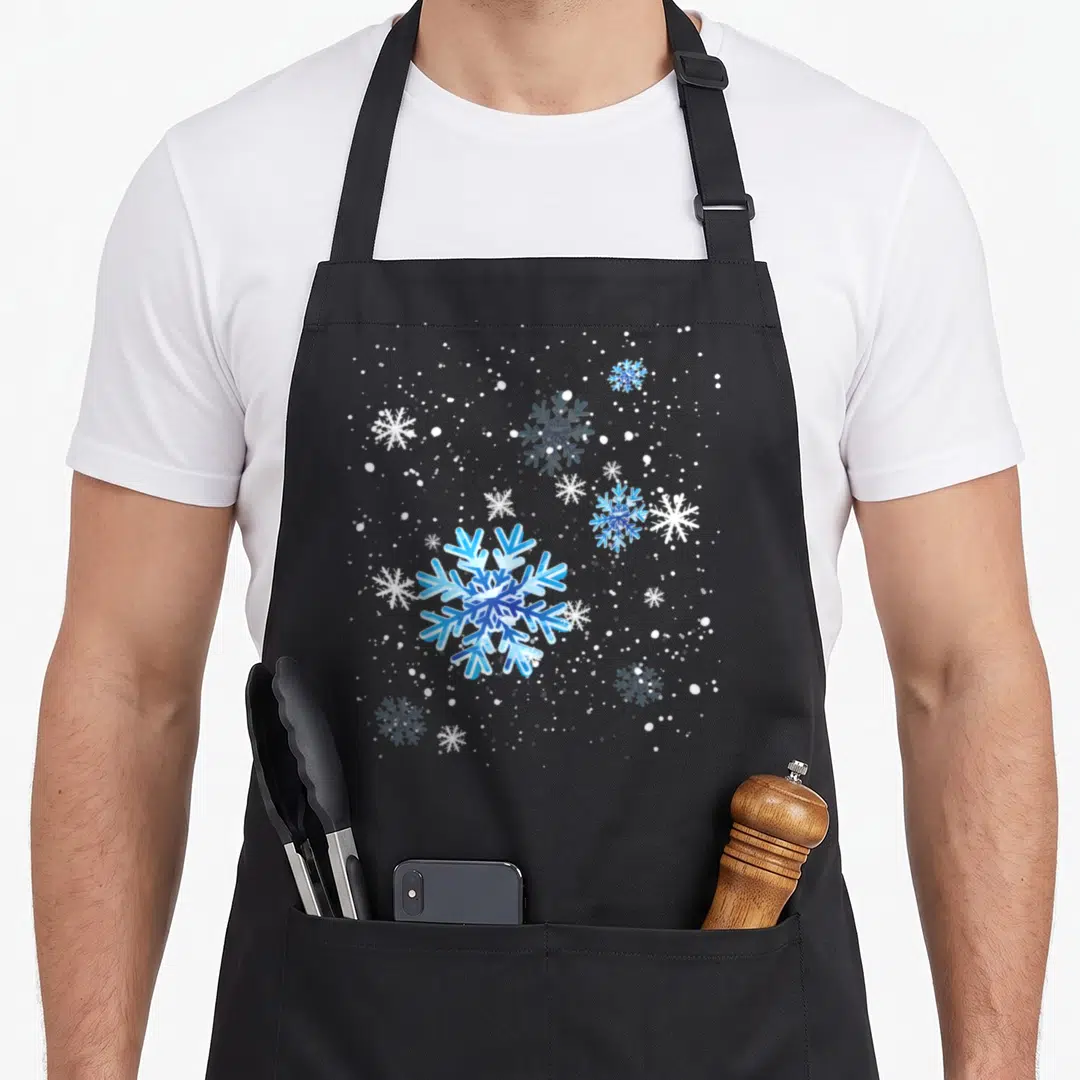 Snowflake winter apron - Large blue and white snowflake centered with smaller snowflakes and scattered white dots — shown on a black cotton canvas apron against a white background