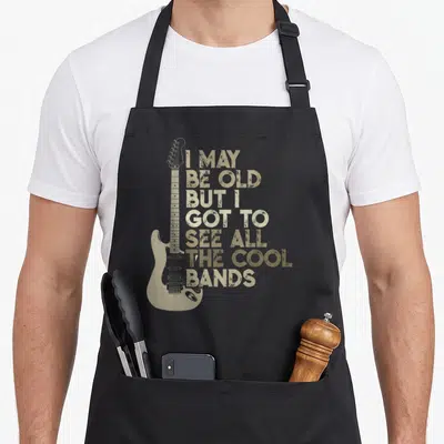 Band may apron - Tan electric guitar next to seven lines of distressed text reading I MAY BE OLD BUT I GOT TO SEE ALL — shown on a black cotton canvas apron against a white background