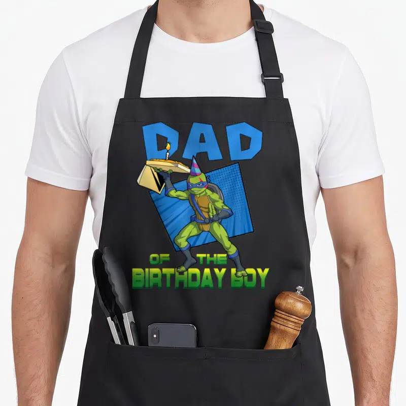 Leo daddy apron - Turtle holding pizza box with dad of the birthday boy text in green blue yellow — shown on a black cotton canvas apron against a white background