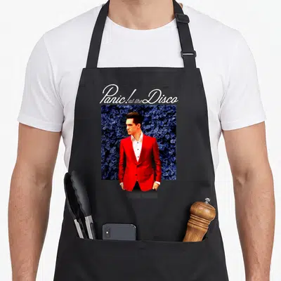 Disco panic attack apron - Panic! at the Disco text above man in red suit against blue leaves — shown on a black cotton canvas apron against a white background