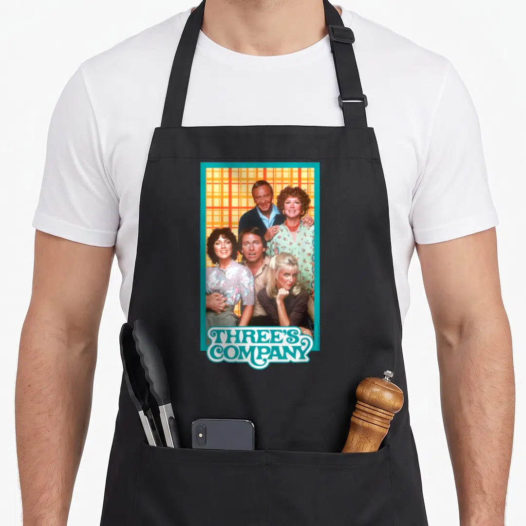 Three 80s apron - Three's Company cast photo with teal logo and orange plaid background — shown on a black cotton canvas apron against a white background