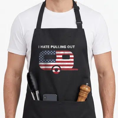 Flag trailer apron - I HATE PULLING OUT text above red white blue star stripe camper trailer — shown on a black cotton canvas apron against a white background