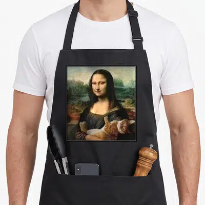 Lisa kitty cat apron - Woman holding orange cat in photo style against landscape background — shown on a black cotton canvas apron against a white background