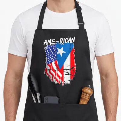Hispanic american flag apron - Arched AME-RICAN text over distressed red white blue graphic merging USA and Puerto — shown on a black cotton canvas apron against a white background