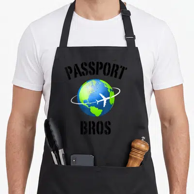 Dating meme apron - PASSPORT BROS text over blue green earth with white airplane orbiting on a ring — shown on a black cotton canvas apron against a white background