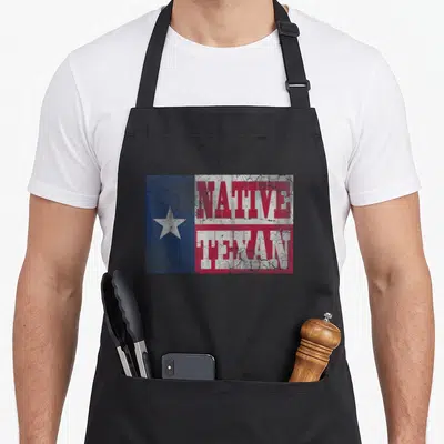 Flag texans apron - Distressed Native Texan text over blue white red Texas flag pattern — shown on a black cotton canvas apron against a white background