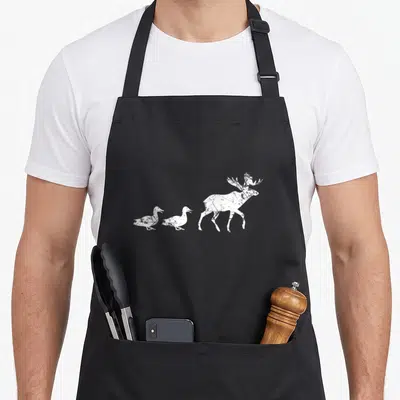 Animal duck apron - White distressed moose silhouette followed by two walking ducks on a black background — shown on a black cotton canvas apron against a white background