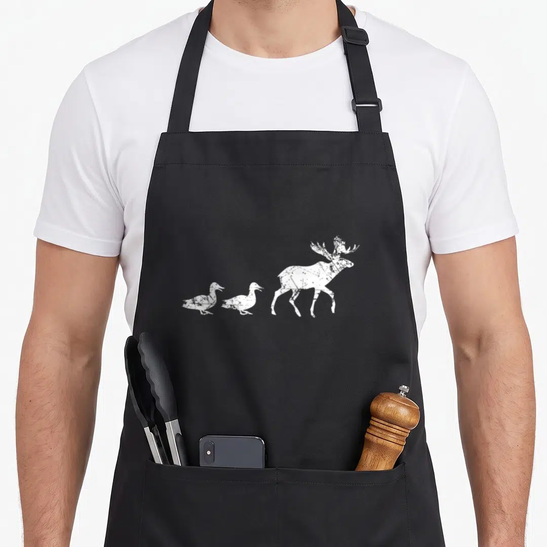 Animal duck apron - White distressed moose silhouette followed by two walking ducks on a black background — shown on a black cotton canvas apron against a white background