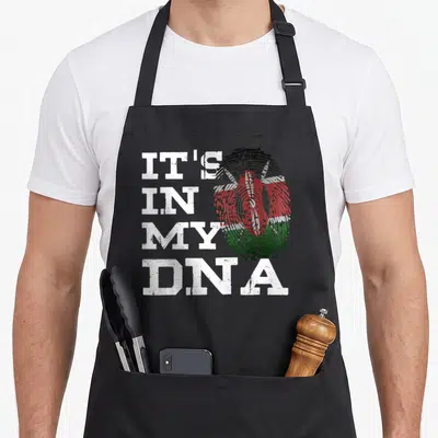 Fingerprint kenyan boy apron - Stacked white text IT'S IN MY DNA next to a distressed fingerprint containing the Kenyan — shown on a black cotton canvas apron against a white background