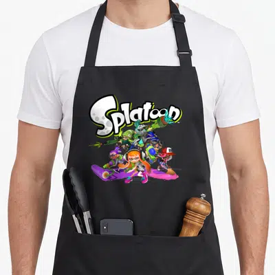 Cute group shot apron - Splatoon logo above Inklings in white green pink blue cartoon action poses — shown on a black cotton canvas apron against a white background