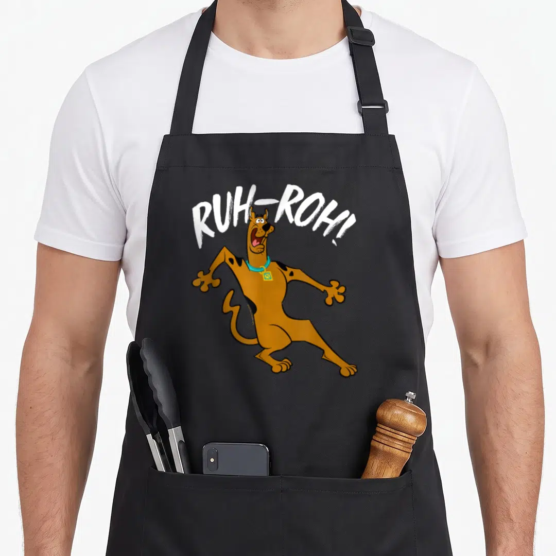 Ruh decade apron - Startled brown Scooby-Doo below arched white RUH-ROH! text — shown on a black cotton canvas apron against a white background