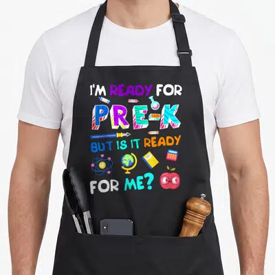 Pre 1st preschool apron - Stacked text I'm Ready for Pre-K surrounded by crayons globe atom and bespectacled apple — shown on a black cotton canvas apron against a white background