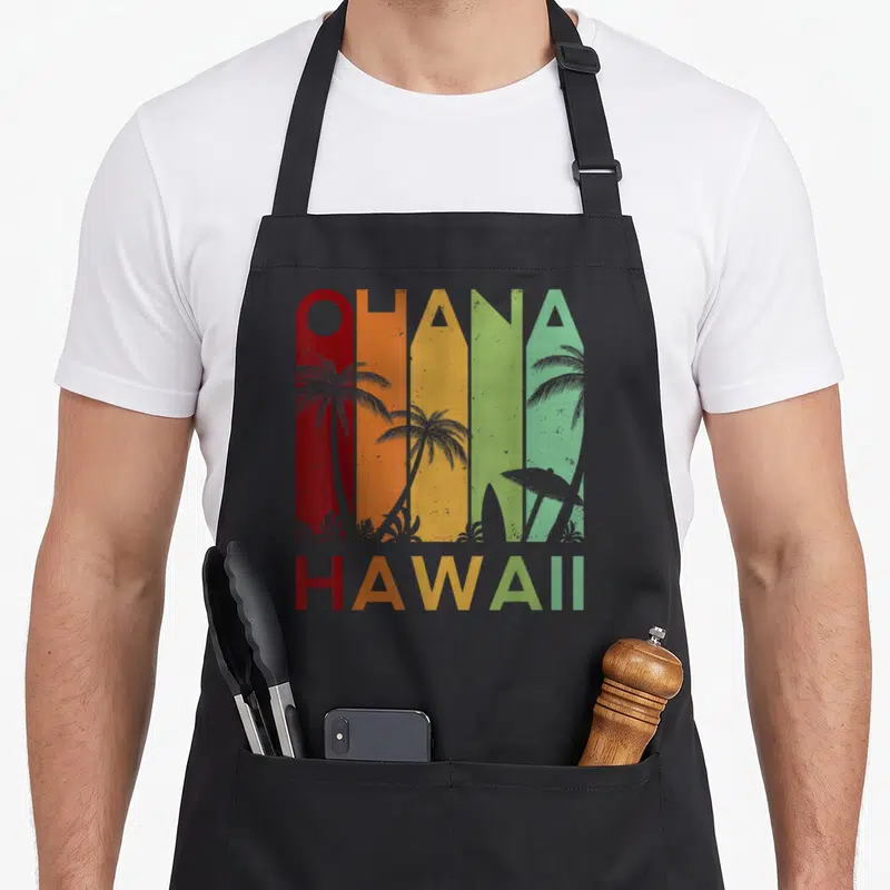 Hawaii family aprons - Retro Ohana Hawaii text with palm trees in red orange yellow and green vertical bands — shown on a black cotton canvas apron against a white background