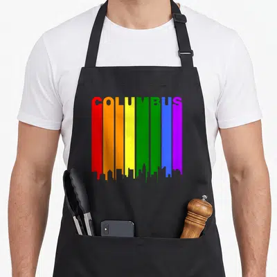 Columbus gay pride apron - Vertical rainbow stripes forming a skyline with COLUMBUS text integrated at the top — shown on a black cotton canvas apron against a white background