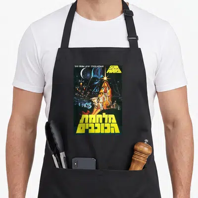 Movie hebrew aprons - Vintage Star Wars poster with Hebrew text, Luke Skywalker, and space ships in yellow and blue — shown on a black cotton canvas apron against a white background
