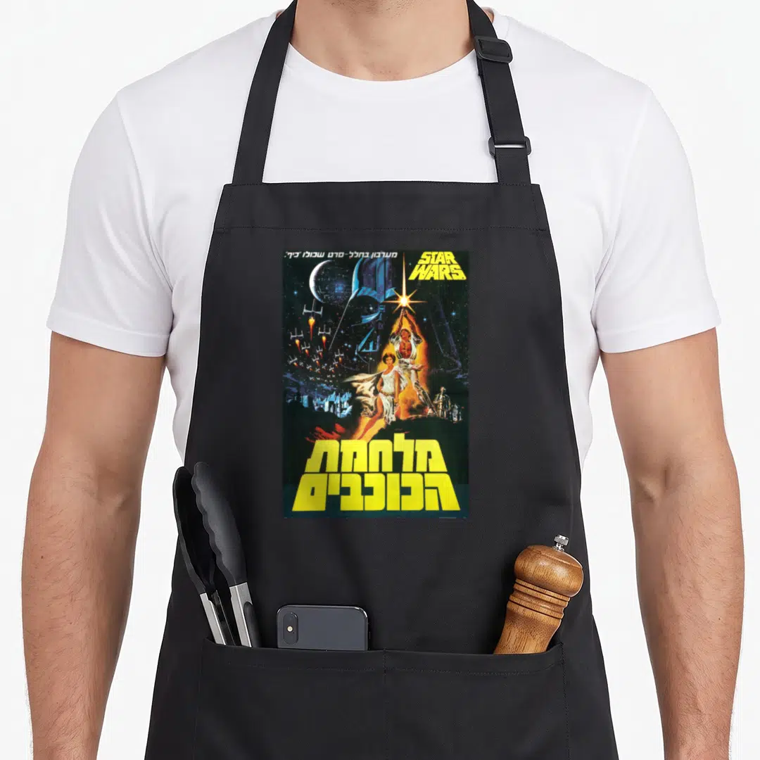 Movie hebrew aprons - Vintage Star Wars poster with Hebrew text, Luke Skywalker, and space ships in yellow and blue — shown on a black cotton canvas apron against a white background