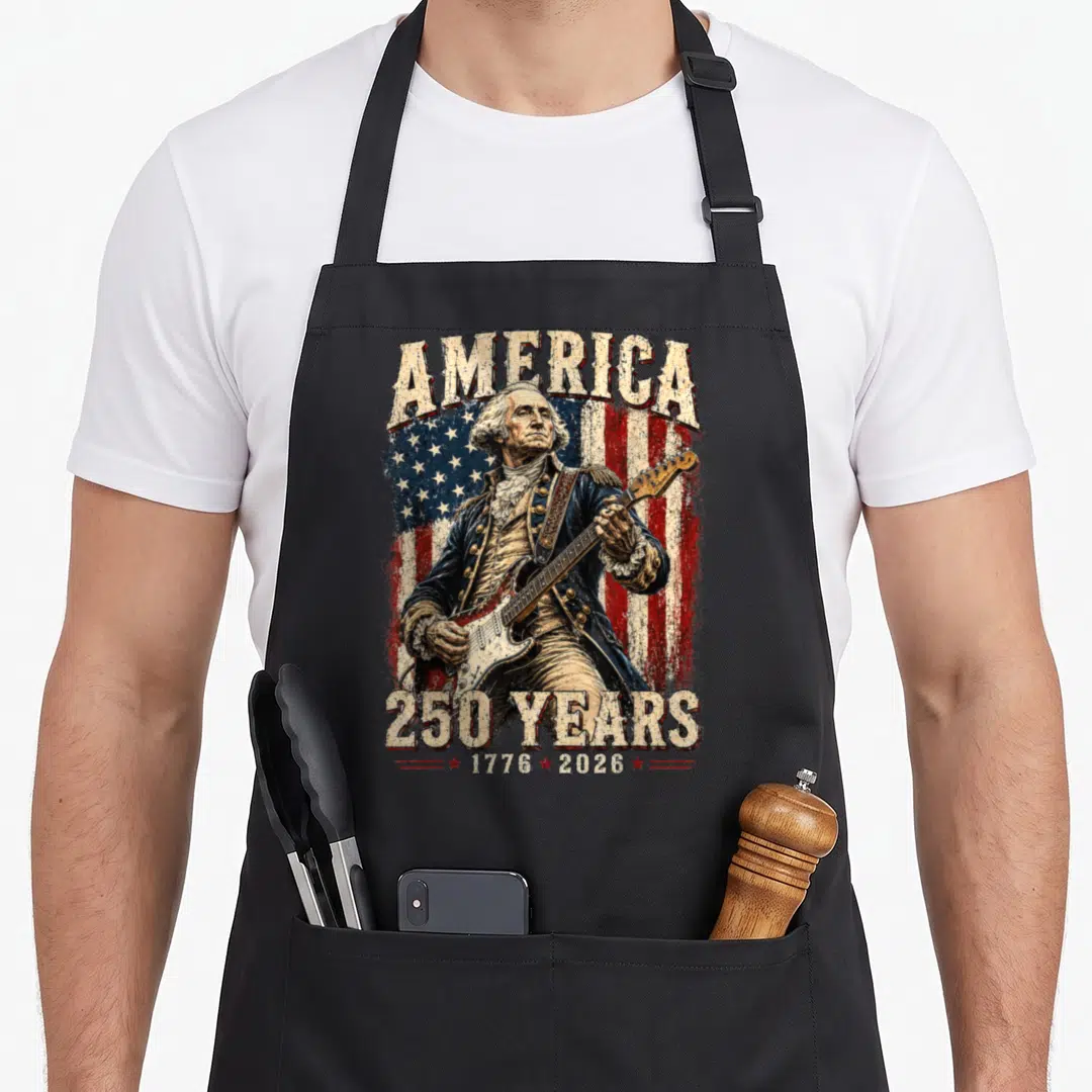 George playing guitar apron - Washington playing guitar in front of distressed flag with America 250 years text — shown on a black cotton canvas apron against a white background