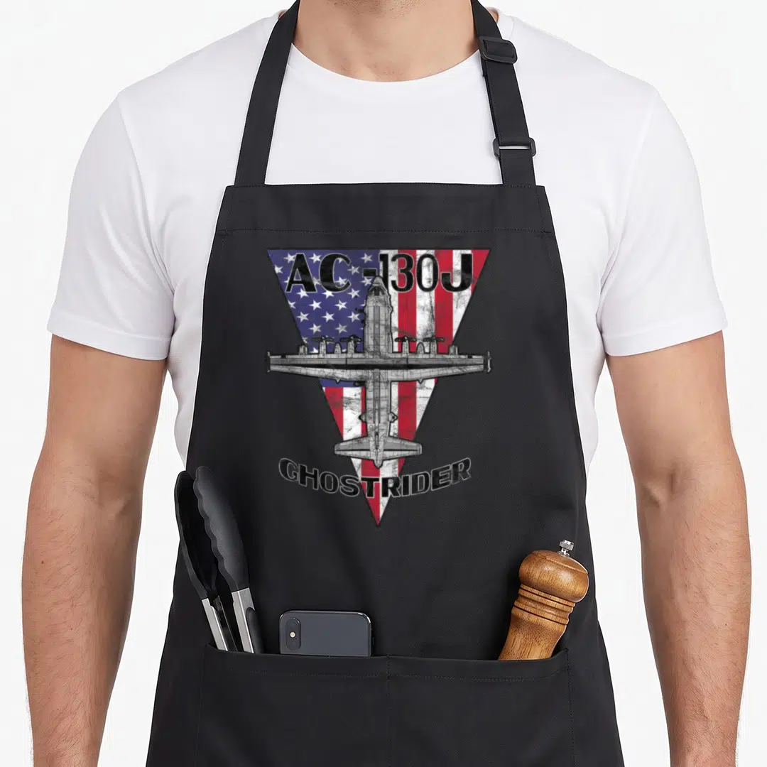 Ghostrider patriotic apron - AC-130J Ghostrider text over distressed inverted US flag triangle with grey aircraft — shown on a black cotton canvas apron against a white background