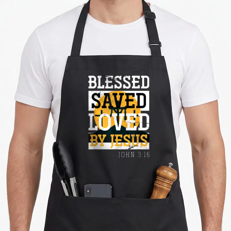 Jesus lord cross apron - Stacked BLESSED SAVED LOVED BY JESUS text over black cross and yellow sun with John 3:16 — shown on a black cotton canvas apron against a white background