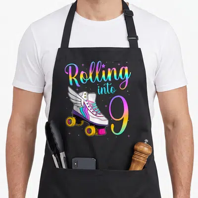 Skate turning apron - Rolling into 9 text with winged roller skate and rainbow gradient stars — shown on a black cotton canvas apron against a white background