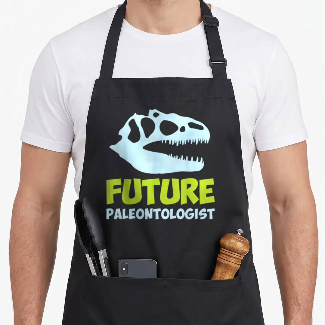 Paleontologist dinosaur science apron - Light blue dinosaur skull above Future Paleontologist text in lime green — shown on a black cotton canvas apron against a white background