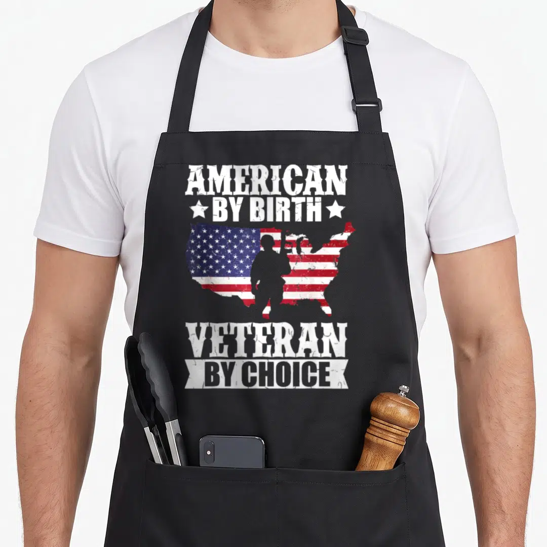 Birth american flag apron - Distressed AMERICAN BY BIRTH VETERAN BY CHOICE text with US flag map and soldier silhouette — shown on a black cotton canvas apron against a white background