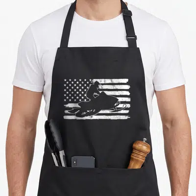 Snowmobile 4th of july apron - White distressed US flag with superimposed snowmobile rider silhouette — shown on a black cotton canvas apron against a white background
