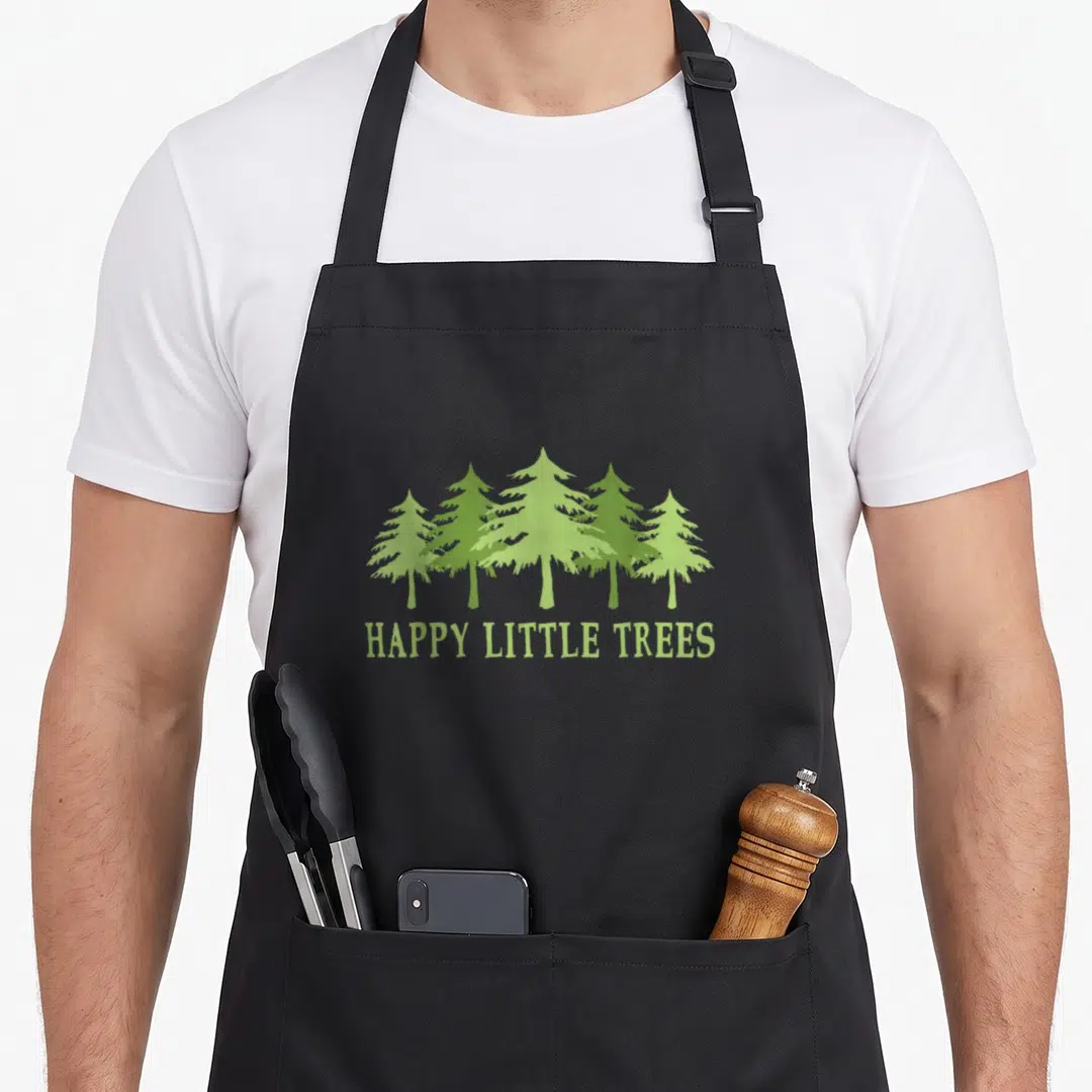 Tree camping apron - Five light green cartoon evergreen trees above HAPPY LITTLE TREES text — shown on a black cotton canvas apron against a white background
