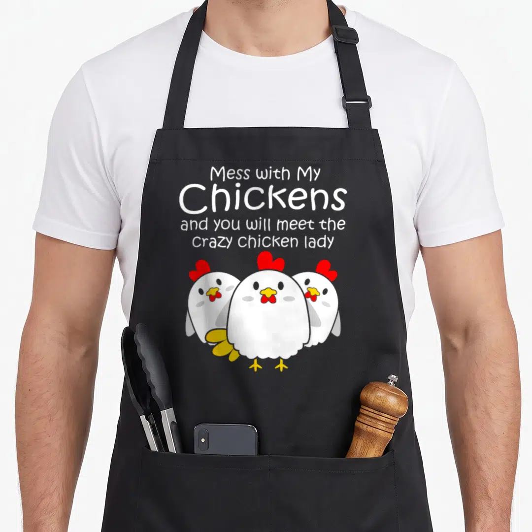 Backyard chicken with apron - Four lines of text above three cartoon white chickens with red combs and yellow beaks — shown on a black cotton canvas apron against a white background
