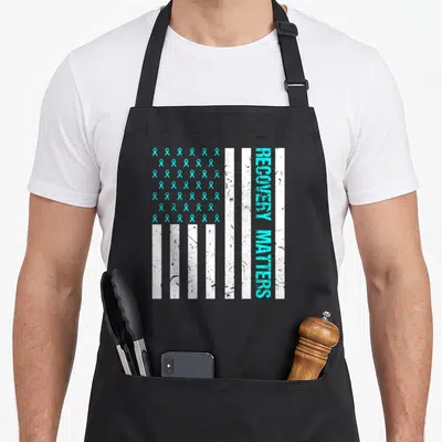 Matter addiction recovery apron - Turquoise ribbons and vertical RECOVERY MATTERS text on distressed white flag stripes — shown on a black cotton canvas apron against a white background