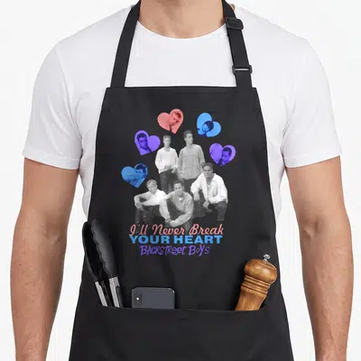Backstreet break apron - Five grayscale men surrounded by four pink blue and purple heart frames with stacked text below — shown on a black cotton canvas apron against a white background