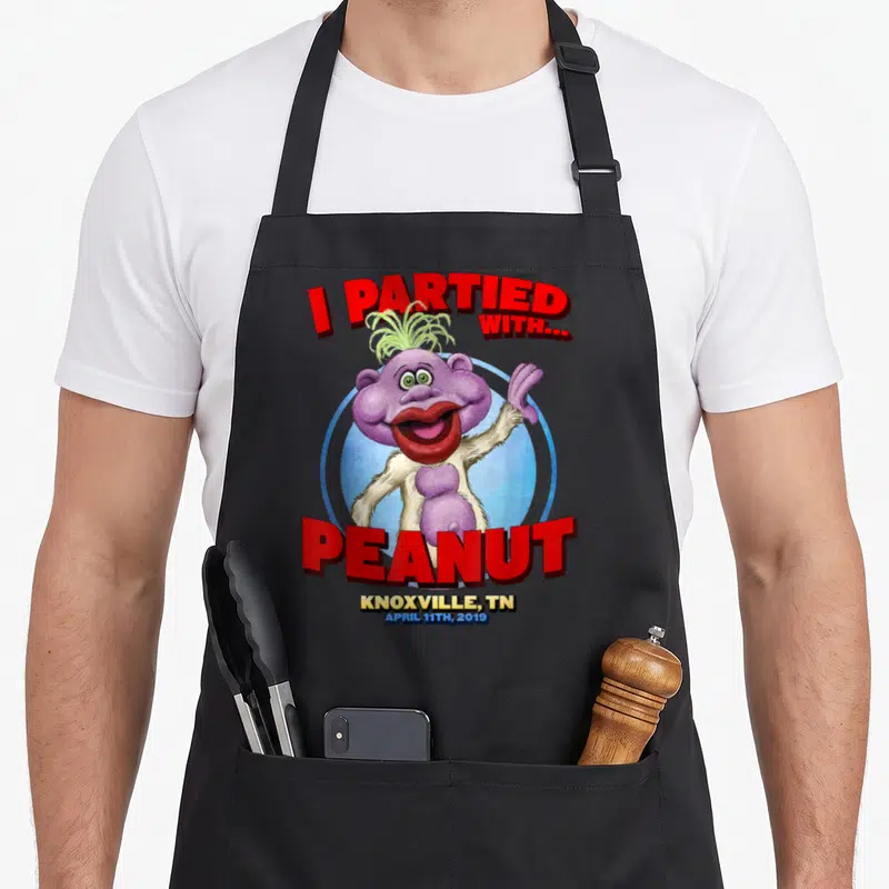 Peanut knoxville apron - Purple monster inside blue circle with red text reading I Partied With Peanut Knoxville TN — shown on a black cotton canvas apron against a white background