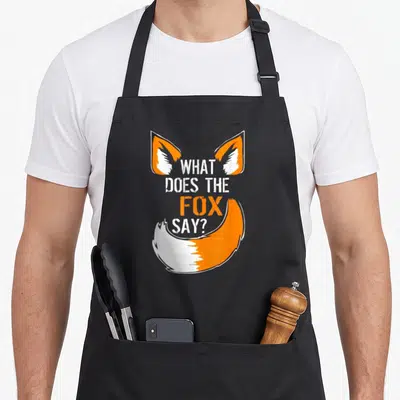 Fox print apron gift - Stacked text what does the fox say framed by orange and white cartoon fox ears and tail — shown on a black cotton canvas apron against a white background