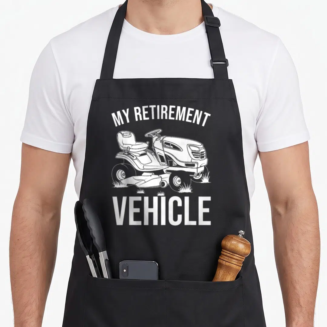 Lawn retirement apron - White line-art of a lawn tractor with arched MY RETIREMENT and bottom VEHICLE text — shown on a black cotton canvas apron against a white background